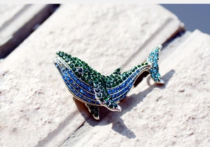 Detailed view of rhinestone whale brooch with gradient blue crystals on stone surface