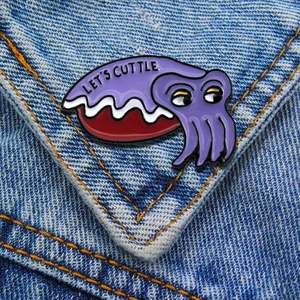 Detail of purple enamel cuttlefish pin with 'LET'S CUTTLE' text on blue denim jacket