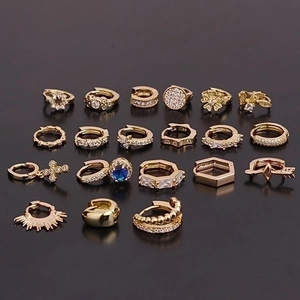 Set of nine pairs of gold geometric huggie earrings with zircons on dark background