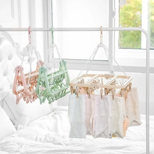 Three foldable drying racks with multiple clips in pink, green, and beige hanging by a window