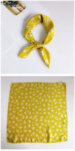 Detail of silk-textured yellow square scarf with white leaf patterns and knotted styling