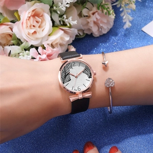 Close-up of black leather strap watch with rose gold bow and heart charm bracelet on wrist