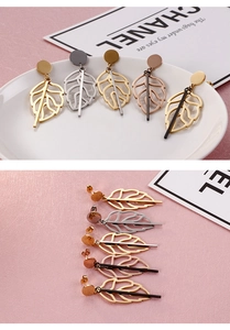 Close-up of elegant leaf-shaped metal earrings in gold and silver on a white plate