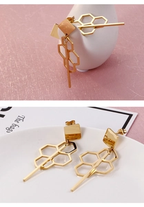 Detailed view of gold earrings with geometric honeycomb pattern and tassel design