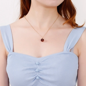 Elegant gold chain necklace with round deep red crystal pendant worn by a model