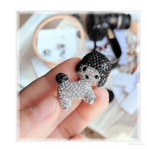 Close-up of poodle brooch with black and white rhinestones held by hand for scale