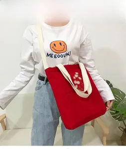 Detail showing red corduroy tote bag with daisy embroidery and white woven shoulder straps