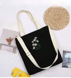 Close-up of delicate daisy flower embroidery on a black corduroy canvas tote bag