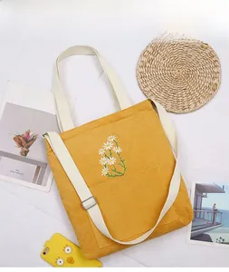 Close-up of yellow corduroy tote bag with white daisy embroidery and front pocket