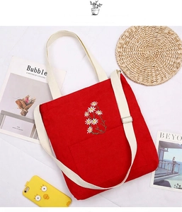 Detail of red corduroy tote with daisy embroidery and adjustable straps on white background
