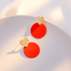 Detailed view of red round drop earrings with textured gold heart studs on ceramic tray