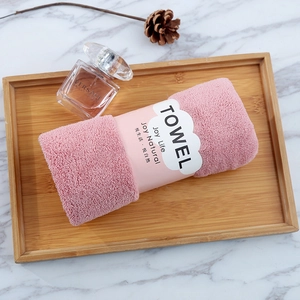 Pink coral fleece towel rolled in a wooden tray on a white marble background surface