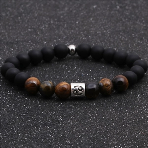 Macro detail of tiger eye and matte black beaded bracelet with Cancer zodiac sign