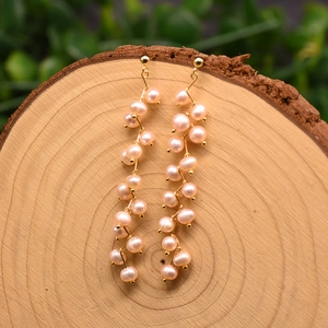 Detail of long 18k gold plated drop earrings with pink freshwater pearls on wood