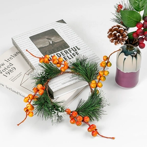 Artificial Christmas wreath and pine needle candle ring with berries on a white table