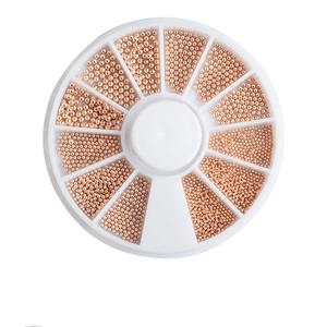 Macro detail of rose gold nail art metal beads in a white circular compartment storage box