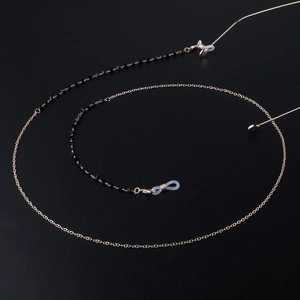 Chaîne de lunettes dorée avec perles de cristal noir sur un fond sombre texturé
