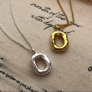 Detail shot of organic irregular donut pendant in gold and silver finish on fabric