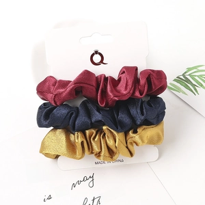 Three-piece set of satin scrunchies in wine red, navy blue, and gold on display card