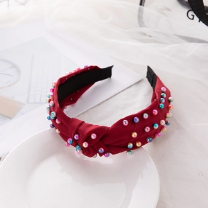 Red knotted pearl headband with colorful beads on white fabric and lace background