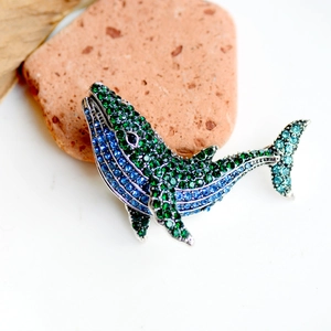 Sparkling whale brooch with blue and green rhinestones on a natural stone base