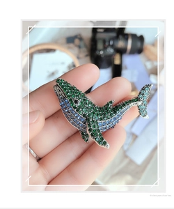 Detail of whale brooch with gradient blue and green crystals held by hand for size check