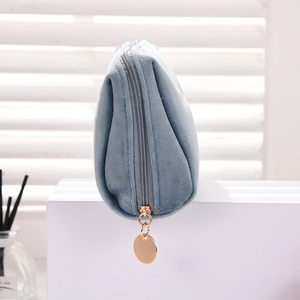 Detail of blue velvet makeup bag featuring gold metal zipper on white display stand