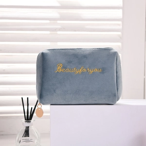 Detail of blue-grey velvet makeup bag with gold embroidery on a white geometric stand