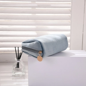 Detail of light blue velvet cosmetic bag featuring a golden round metal zipper puller