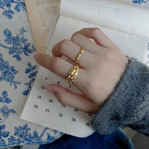Detailed view of two irregular lava textured gold rings worn on a hand with vintage accents