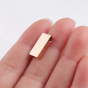 Close-up of a small gold-finished rectangular metal pendant bead held on a fingertip