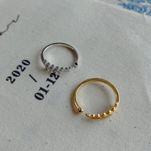 Detail view of gold and silver leaf pattern open rings on minimalist linen fabric