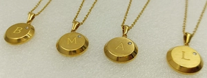 Detail of four gold-plated stainless steel necklaces with round letter pendants B, M, A, L