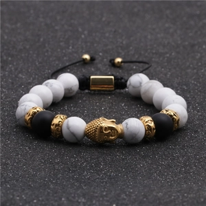 Dettaglio macro del ciondolo testa di Buddha dorata e perle marmoree su bracciale intrecciato