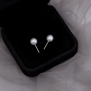 Macro shot of elegant white pearl stud earrings resting on black velvet with grey tulle