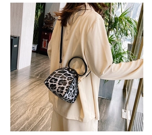 Detail of leopard print triangle bag with black circular handle on beige blazer