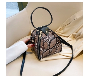 Detailed macro view of snake print triangular bag featuring a black round handle and metal zipper