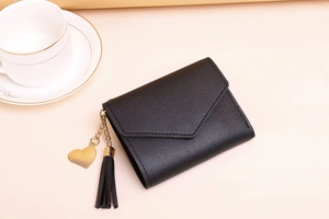 Detail of black tri-fold wallet featuring lychee grain leather, heart charm and tassel