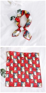 Detail of red square silk scarf featuring cute cat print on a white linen surface