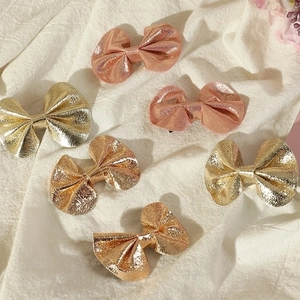 Close-up of metallic bow hair clips in gold and bronze on a white fabric background
