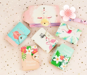 Flat lay of multiple PU leather card holders with floral and flamingo prints on pink fabric