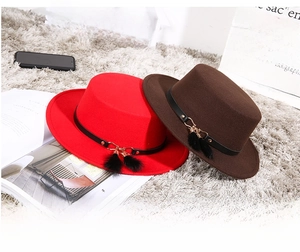 Close-up of felt flat top boater hats with leather bands and fur ball charms on a cozy rug