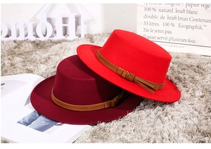 Close-up of stylish flat top wool felt hats in red and burgundy with leather belt detail