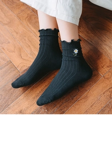 Detailed view of black crew socks with ruffled cuffs and delicate daisy embroidery