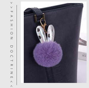 Detail of purple plush bunny ear keychain hanging on a navy blue leather tote bag
