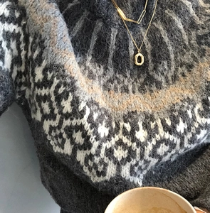 Close-up of Nordic jacquard wool sweater texture with elegant oval donut silver necklace