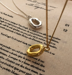 Detail of organic oval pendants in gold and silver finish on vintage script paper