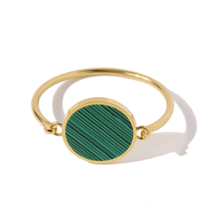 Close-up of gold bangle featuring a circular green malachite inlay on a white backdrop