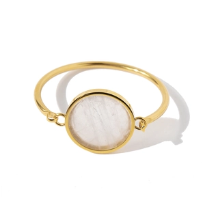 Detail view of a gold bangle featuring a round white mother-of-pearl inlay on white background