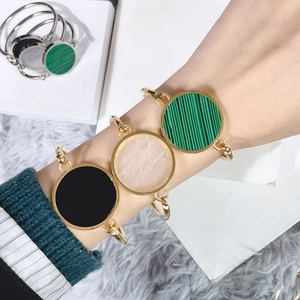 Detailed view of three gold bracelets featuring malachite, black, and white shell charms
